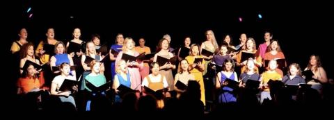 Les membres de la chorale, habillées en couleurs voyants, chantent devant un rideau noir